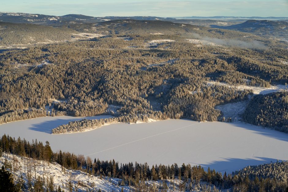 A stunning aerial shot of snowy mountains and a frozen lake under clear skies, showcasing winter's beauty.
