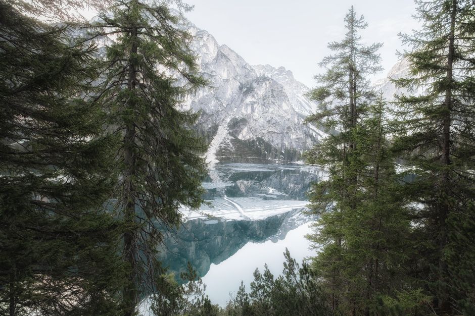 A peaceful winter scene of a mountain lake surrounded by snow-covered trees and majestic peaks.