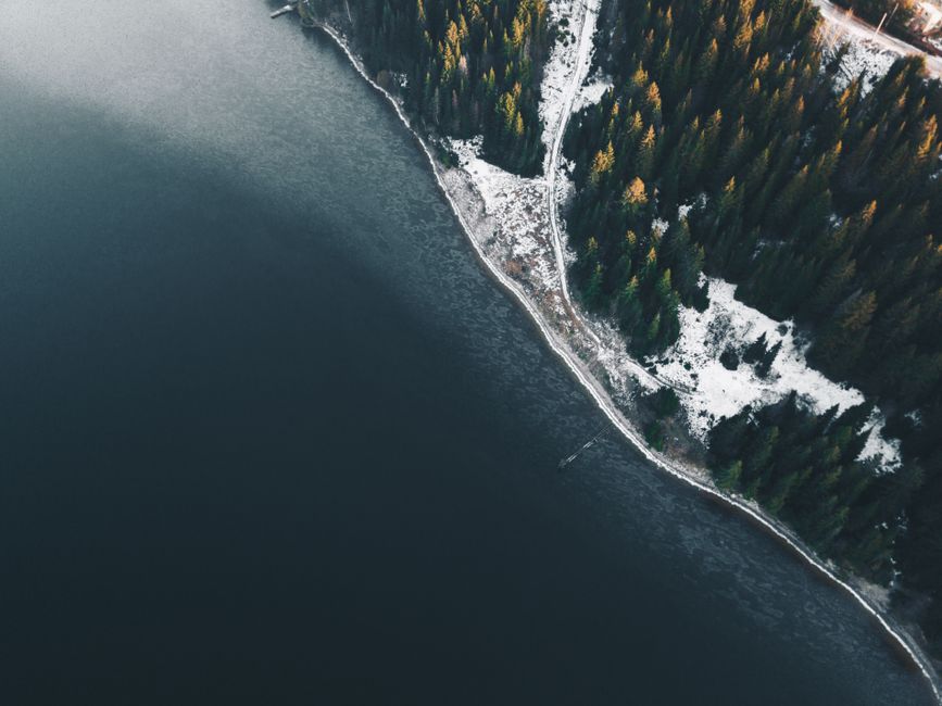 A stunning aerial view of a winter landscape featuring a snow-covered forest along a serene riverbank.