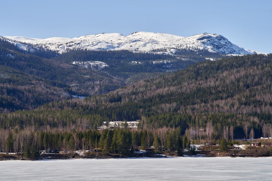 Scenic winter landscape with snow-covered mountains and frozen lake surrounded by evergreen forest.